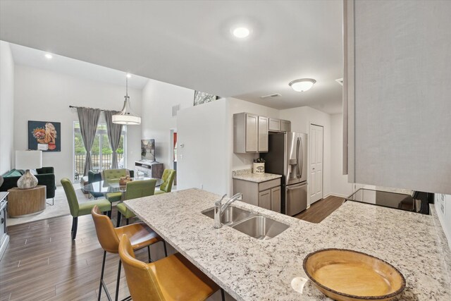 kitchen featuring a sink, stainless steel refrigerator with ice dispenser, gray cabinetry, dark wood-type flooring, and a breakfast bar