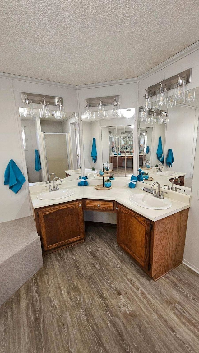 bathroom with wood finished floors, a textured ceiling, double vanity, and a shower stall