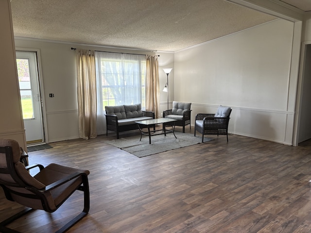 living area featuring a textured ceiling, ornamental molding, wood finished floors, and baseboards