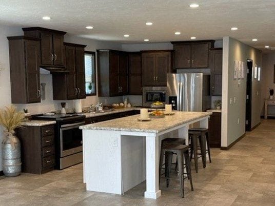 kitchen with stainless steel appliances, dark brown cabinetry, a center island, a breakfast bar, and recessed lighting