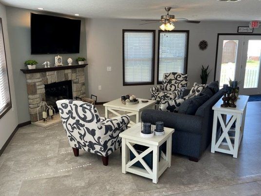 living room featuring healthy amount of natural light, a stone fireplace, ceiling fan, and baseboards