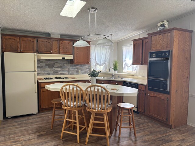 kitchen with white appliances, a sink, a skylight, under cabinet range hood, and a textured ceiling