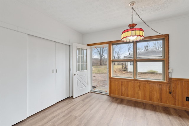 unfurnished dining area featuring a wealth of natural light, wood walls, wainscoting, and light wood-type flooring