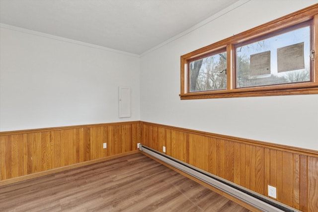 unfurnished room with a baseboard heating unit, ornamental molding, wainscoting, wood walls, and wood finished floors
