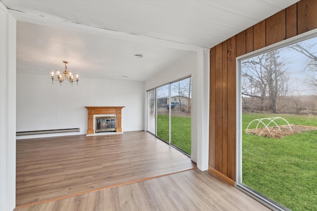 unfurnished living room with light wood finished floors, a notable chandelier, a glass covered fireplace, wooden walls, and a baseboard radiator
