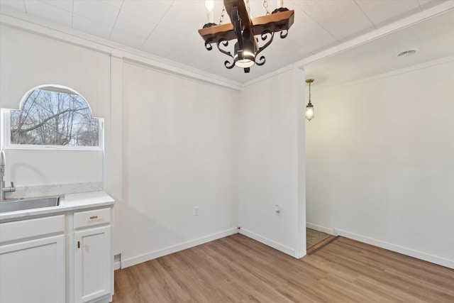 unfurnished dining area featuring a sink, crown molding, light wood-type flooring, baseboards, and a chandelier