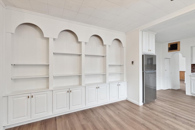 unfurnished living room featuring crown molding, built in features, light wood-style flooring, and baseboards