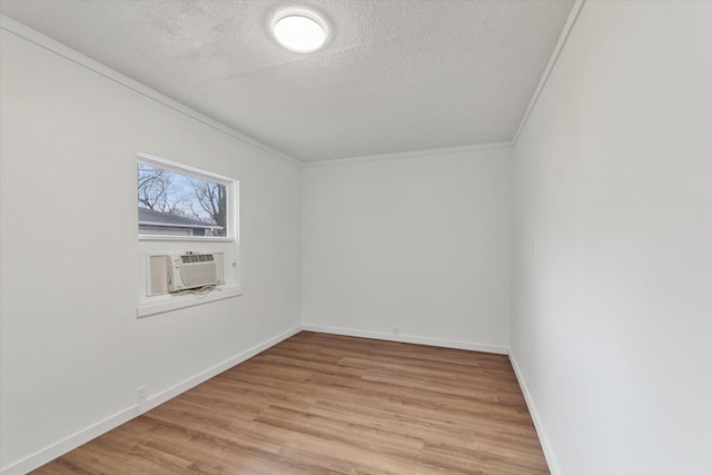 spare room with light wood-style flooring, a textured ceiling, baseboards, cooling unit, and crown molding