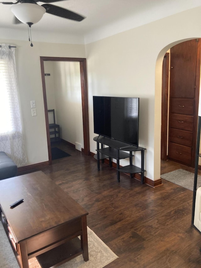 living room featuring arched walkways, baseboards, ceiling fan, and wood finished floors