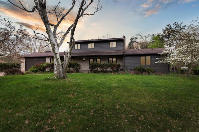 rear view of property featuring a garage, a chimney, and a lawn