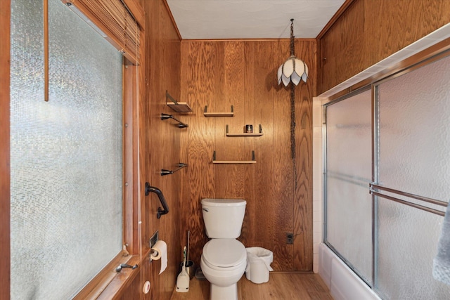 bathroom featuring toilet, wooden walls, wood finished floors, and shower / bath combination with glass door
