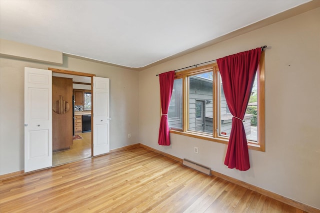 spare room featuring a baseboard heating unit, light wood-style floors, and baseboards