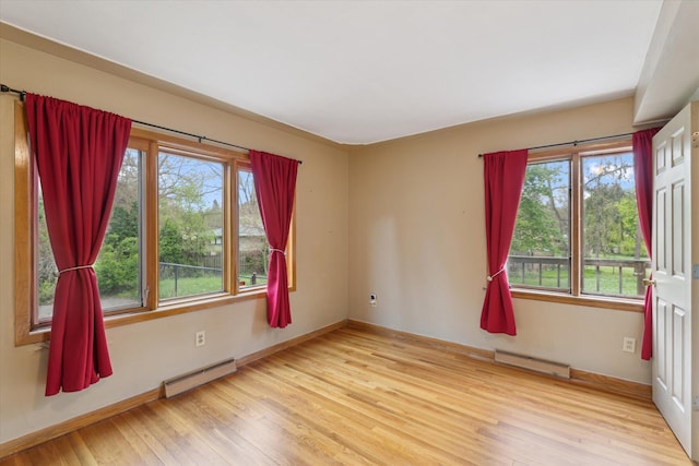 spare room featuring a baseboard heating unit, plenty of natural light, and wood finished floors