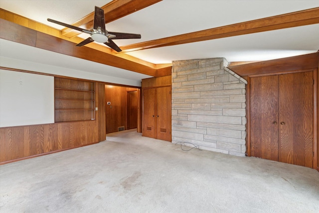 carpeted empty room with wooden walls, a ceiling fan, and beamed ceiling