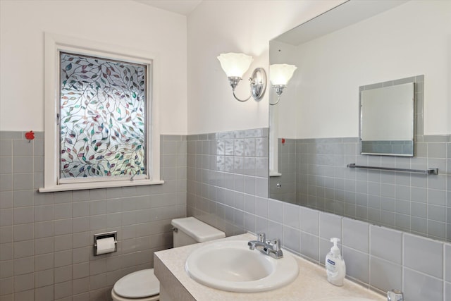 bathroom featuring toilet, tile walls, vanity, and wainscoting