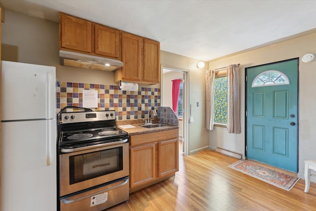 kitchen featuring a sink, freestanding refrigerator, under cabinet range hood, stainless steel electric range oven, and tasteful backsplash