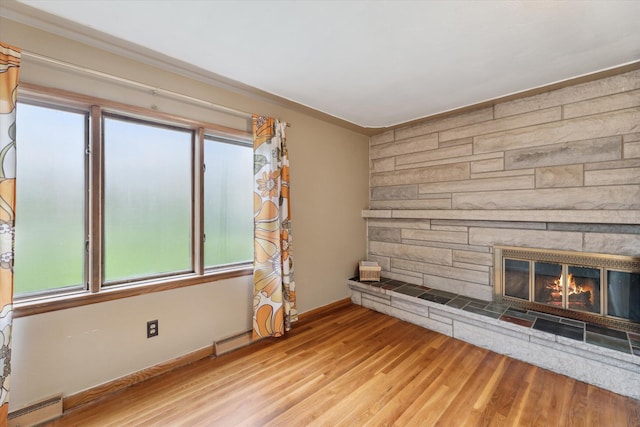 unfurnished living room featuring a baseboard heating unit, a stone fireplace, ornamental molding, light wood finished floors, and baseboards