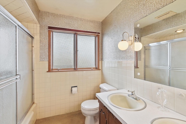 bathroom featuring double vanity, toilet, a sink, tile walls, and bath / shower combo with glass door