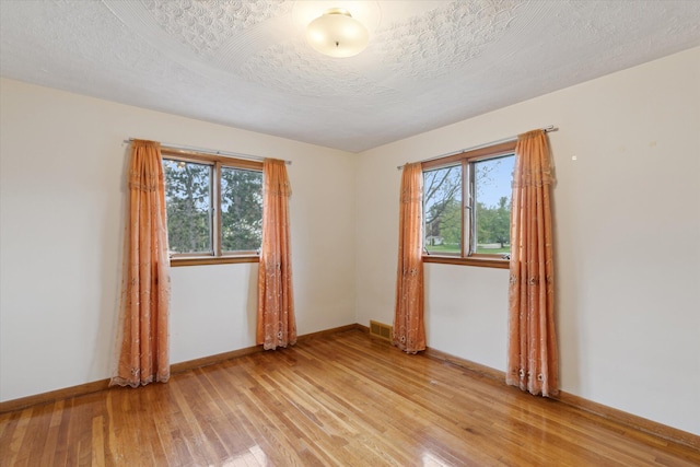 spare room featuring light wood-style floors, plenty of natural light, baseboards, and visible vents