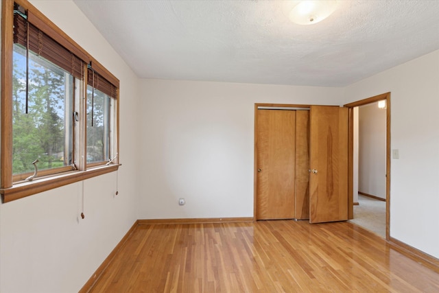 unfurnished bedroom featuring light wood-style flooring, baseboards, and a closet