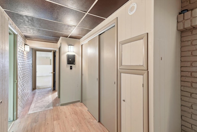 hallway with light wood-style floors and brick wall