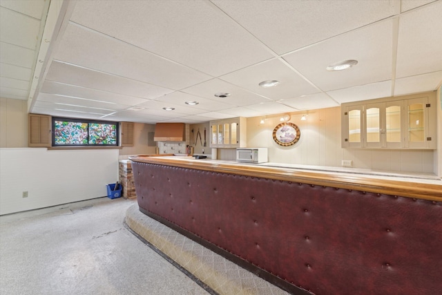 interior space featuring a drop ceiling, carpet flooring, and glass insert cabinets