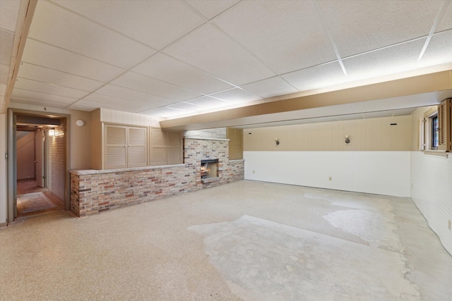 finished below grade area featuring brick wall, a brick fireplace, carpet floors, and a drop ceiling