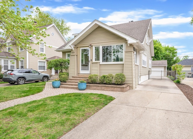 bungalow featuring a detached garage, an outdoor structure, a shingled roof, and a front yard