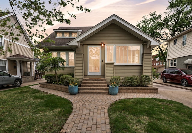 bungalow-style house with entry steps, a shingled roof, and a front yard