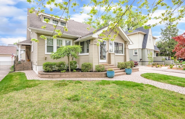 bungalow-style home with a front yard, an outbuilding, a shingled roof, and entry steps