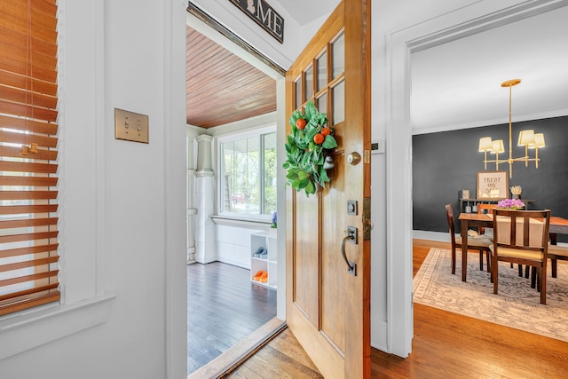 entryway with crown molding, a chandelier, and wood finished floors