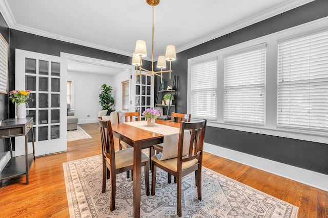 dining area with light wood finished floors, crown molding, baseboards, and a notable chandelier