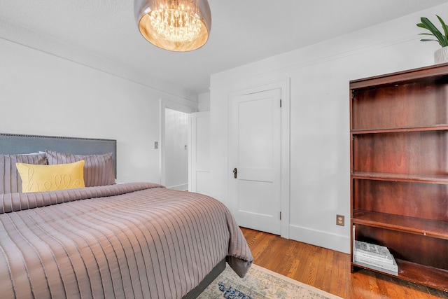 bedroom with baseboards, a notable chandelier, and wood finished floors