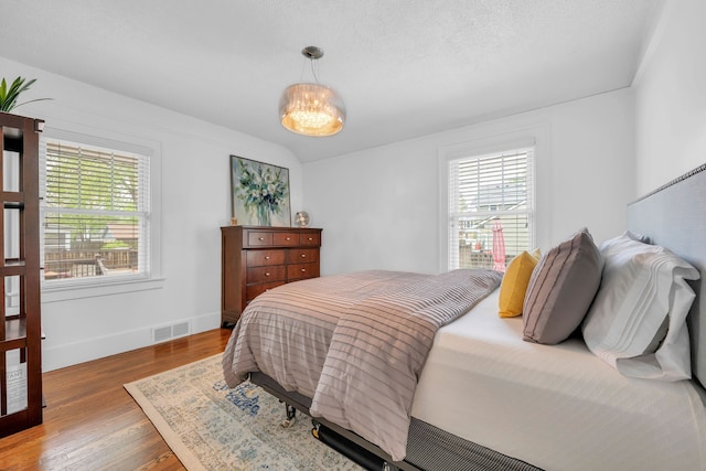 bedroom with baseboards, multiple windows, visible vents, and wood finished floors