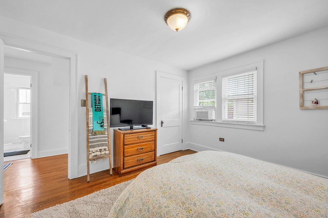bedroom with cooling unit, wood finished floors, and baseboards