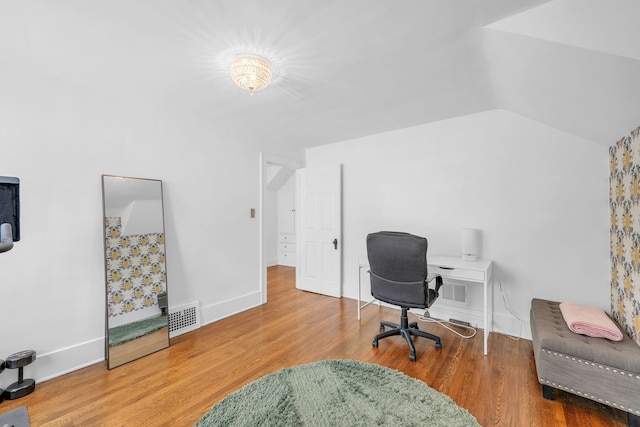 office space with baseboards, vaulted ceiling, wood finished floors, and visible vents