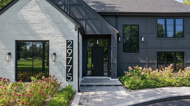 view of exterior entry with a shingled roof and brick siding