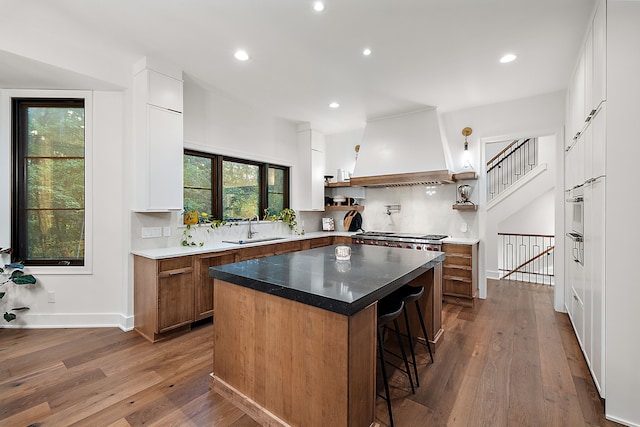 kitchen with a kitchen bar, a sink, open shelves, brown cabinetry, and custom range hood