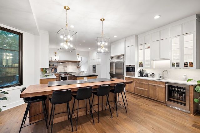 kitchen with a sink, high end appliances, brown cabinetry, a kitchen island, and wine cooler