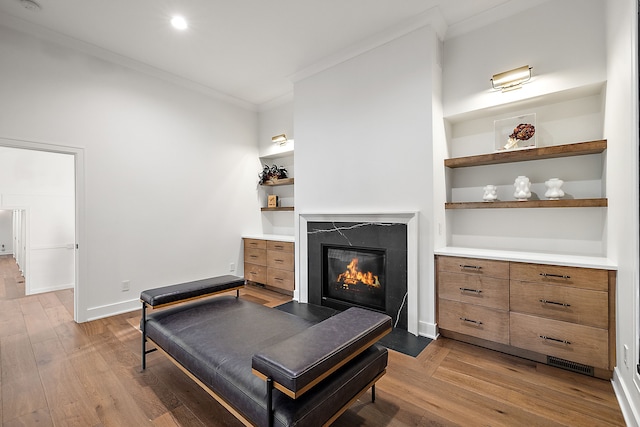 living area featuring a premium fireplace, crown molding, built in features, and wood finished floors