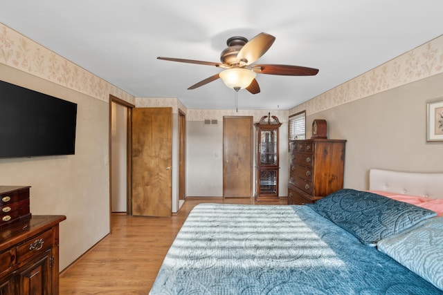 bedroom featuring visible vents, a ceiling fan, wallpapered walls, and light wood-style floors