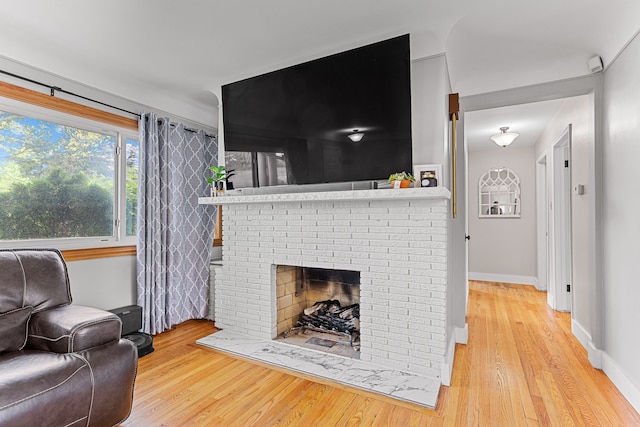 living room featuring wood finished floors, baseboards, and a brick fireplace
