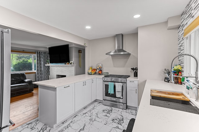 kitchen with marble finish floor, a peninsula, gas stove, and wall chimney exhaust hood