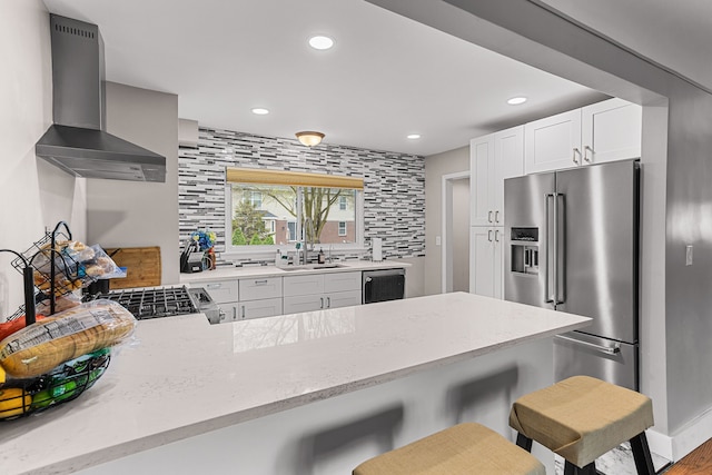 kitchen with light stone countertops, a sink, a kitchen bar, wall chimney exhaust hood, and stainless steel appliances