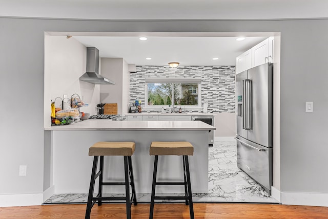 kitchen featuring high end fridge, a breakfast bar, a sink, a peninsula, and wall chimney exhaust hood