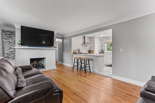 living room with light wood-style flooring, a brick fireplace, and baseboards
