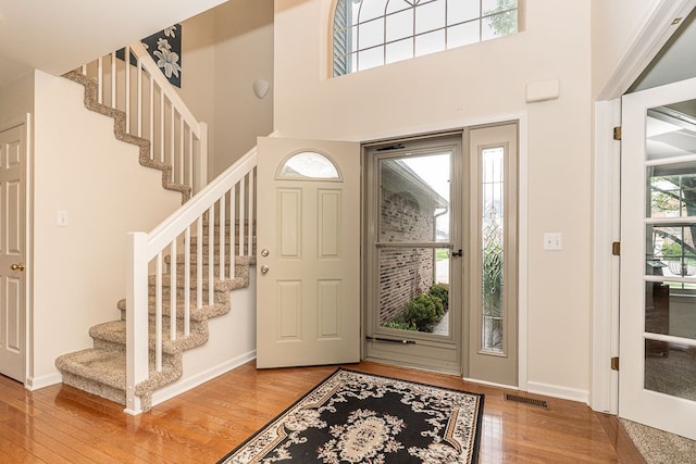 entryway with wood finished floors, stairs, a high ceiling, and baseboards