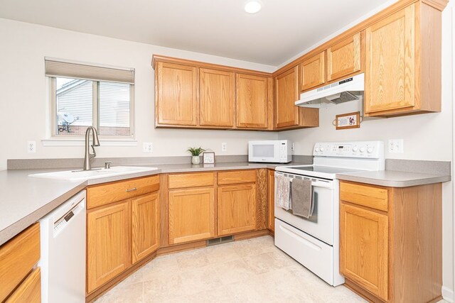 kitchen featuring white appliances, under cabinet range hood, a sink, and light countertops