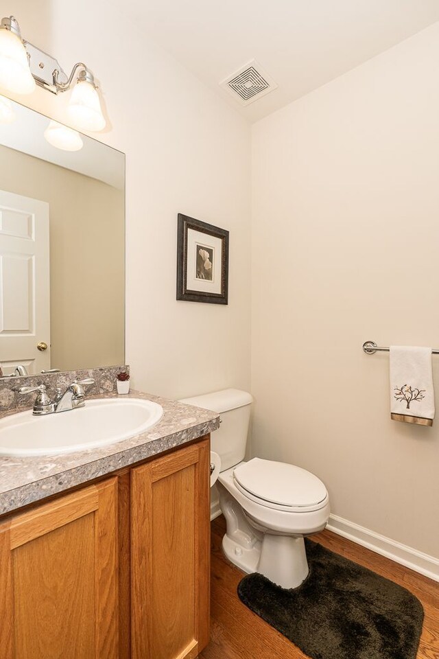 half bathroom with toilet, wood finished floors, vanity, and baseboards
