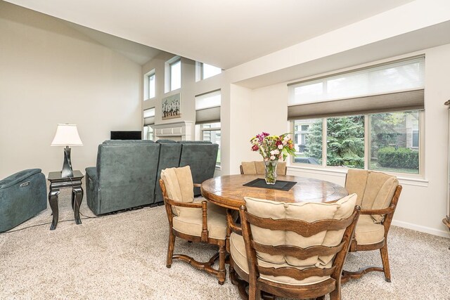 dining space with light colored carpet, a fireplace, and baseboards